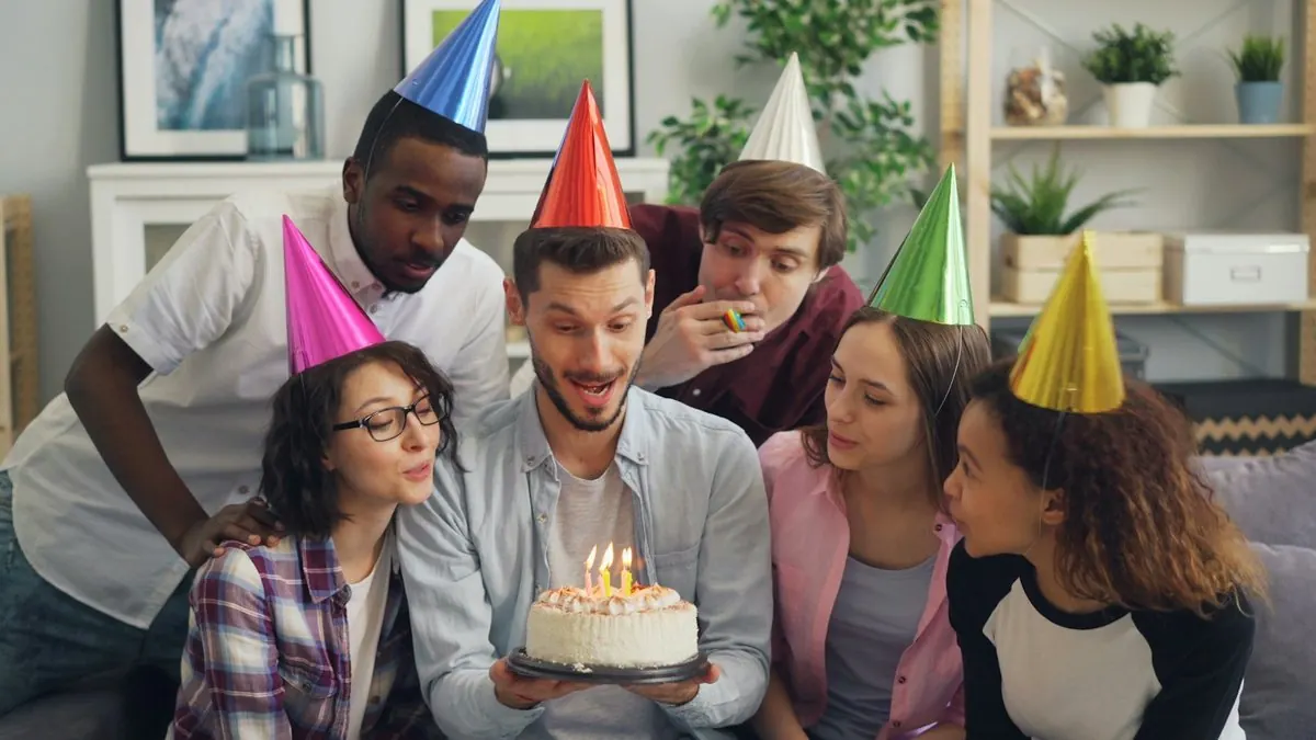 Friends in party hats around a cake, in a living room