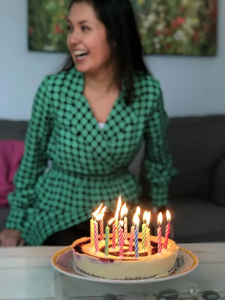 A woman smiles in front of her birthday cake with lit candles