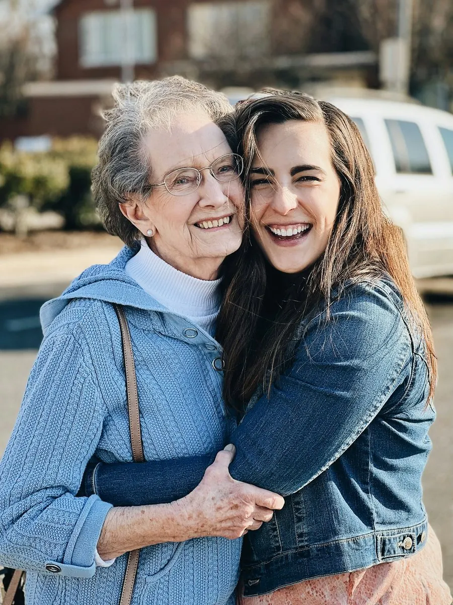 Une grand-mère et sa petite-fille adulte, enlacées et souriantes