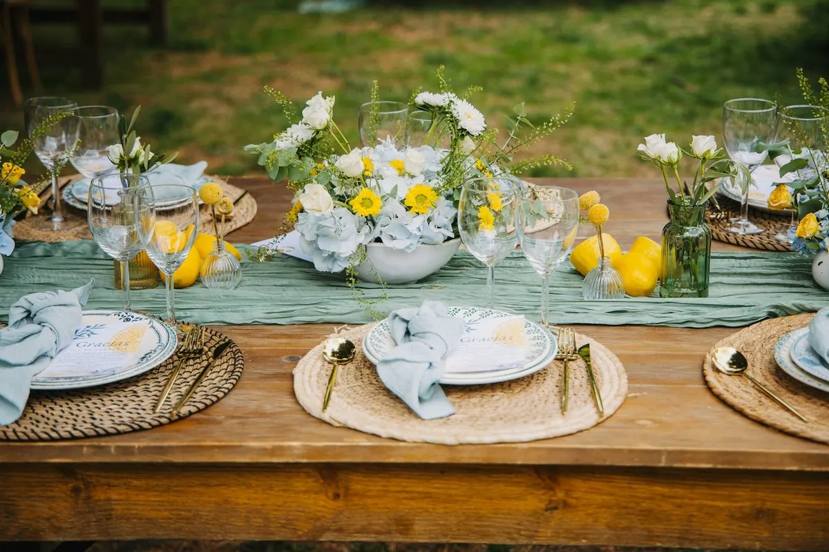 Une longue table de déjeuner dressée dans un jardin, fleurs jaunes et serviettes vert d'eau