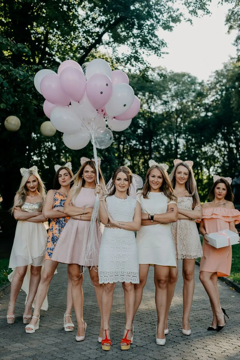 Une bande d'amies en robes blanches marche avec des ballons roses