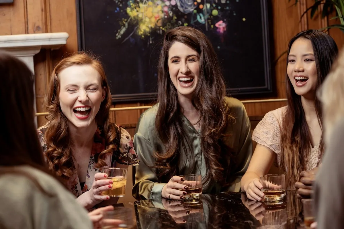 Trois amies éclatent de rire autour d'une table, dans un bar
